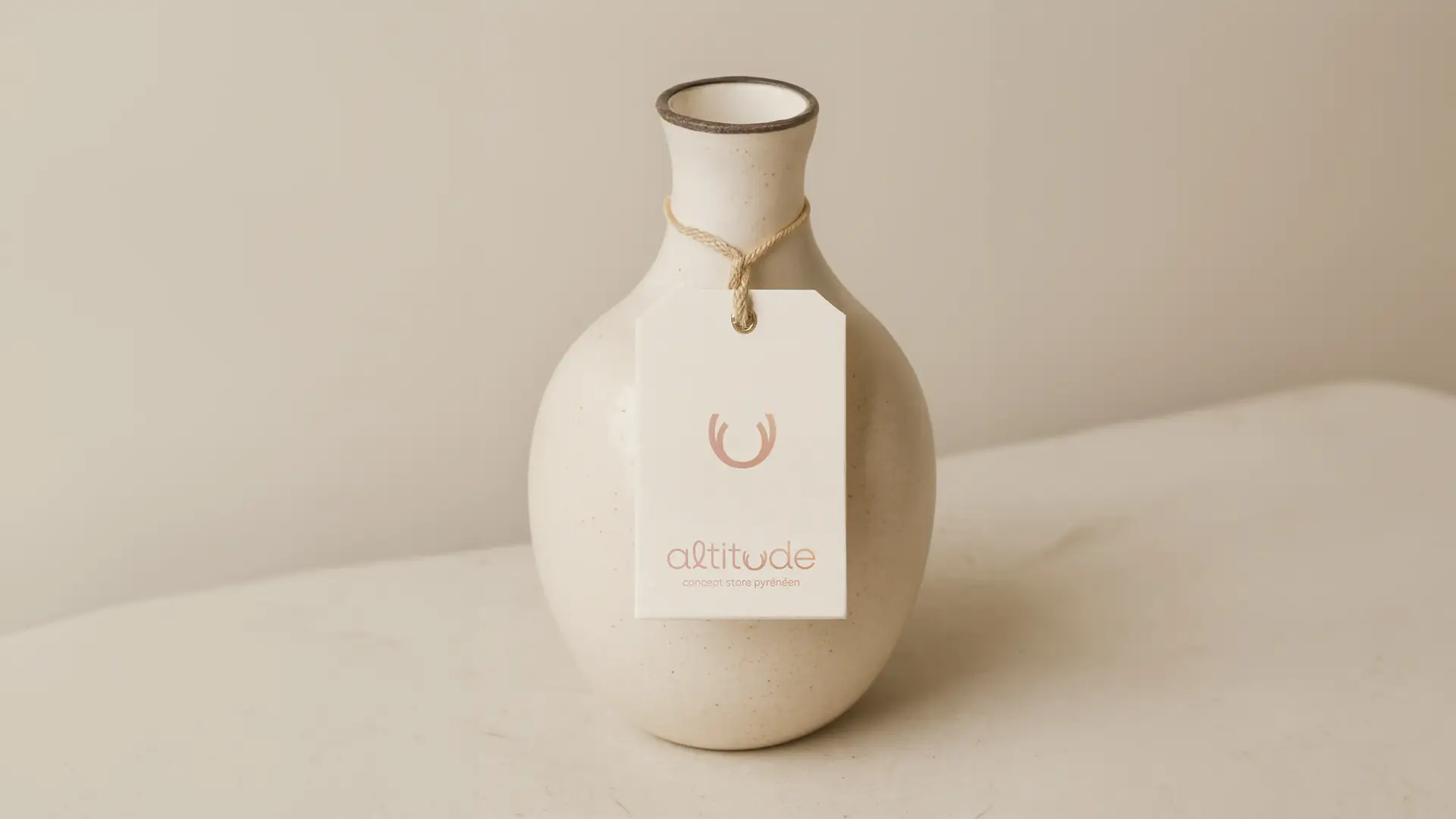 Maquette de vase Altitude avec une étiquette en papier portant le logo minimaliste de la marque, posé sur une surface neutre.