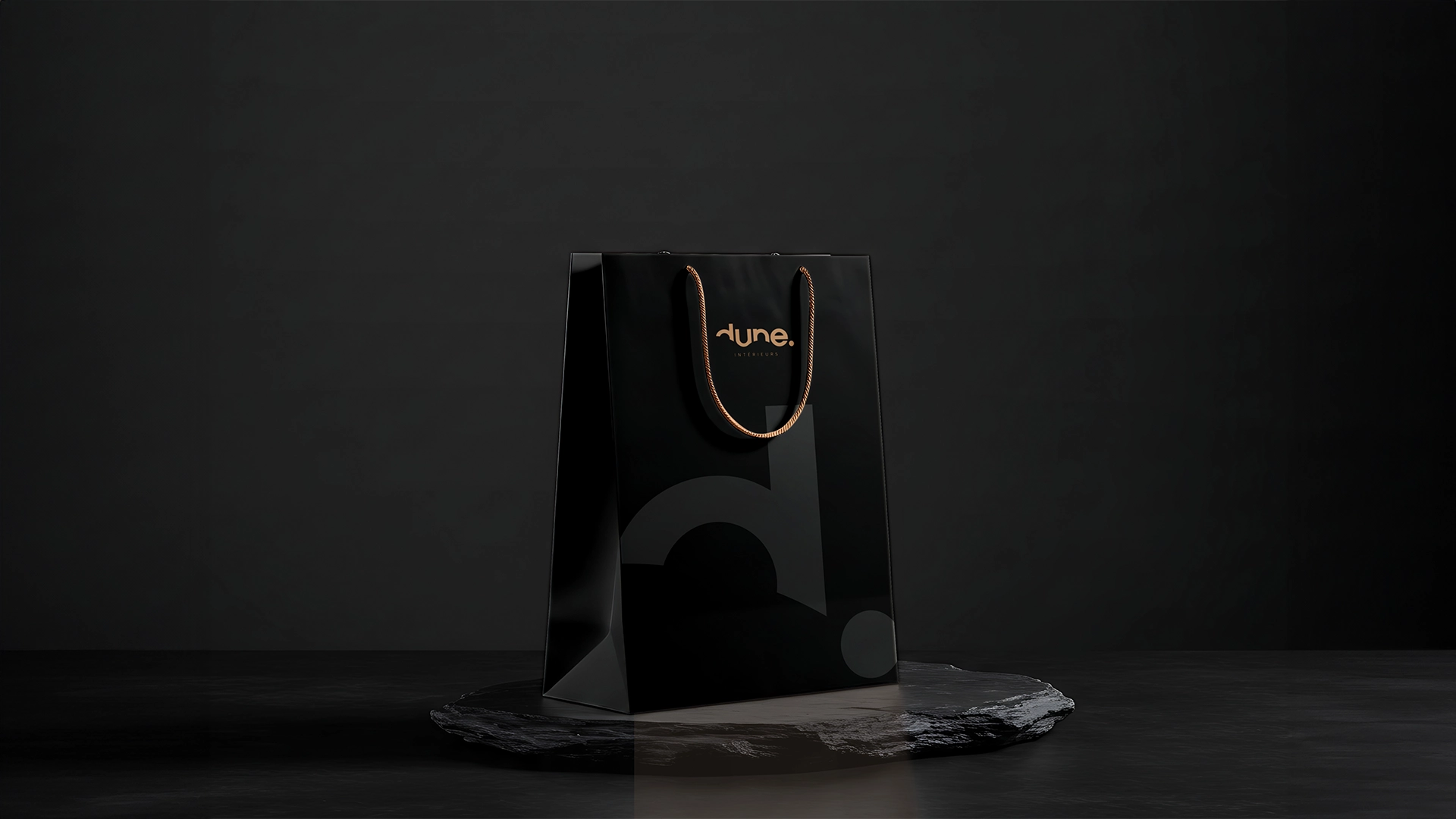 Maquette de sac de shopping noir de la marque dune, avec logo doré et design minimaliste, posé sur une surface en pierre.
